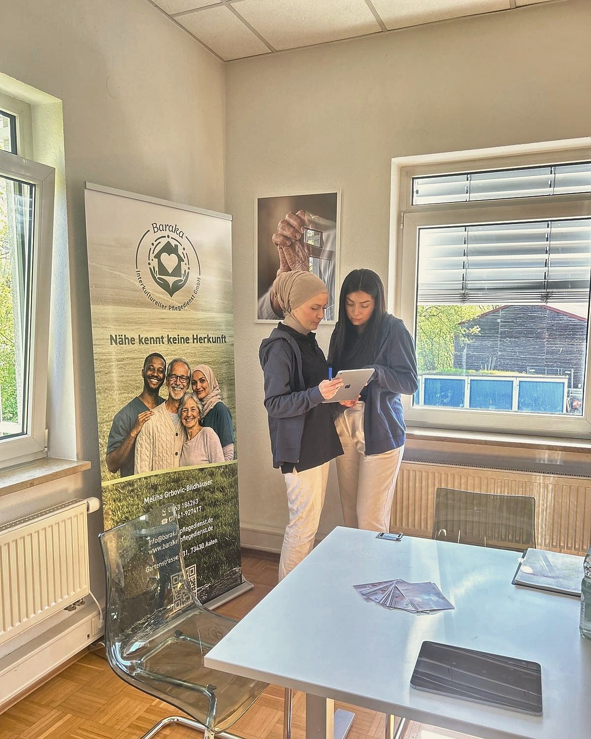 Baraka-Pflegeteam im Büro mit Roll-up „Nähe kennt keine Herkunft