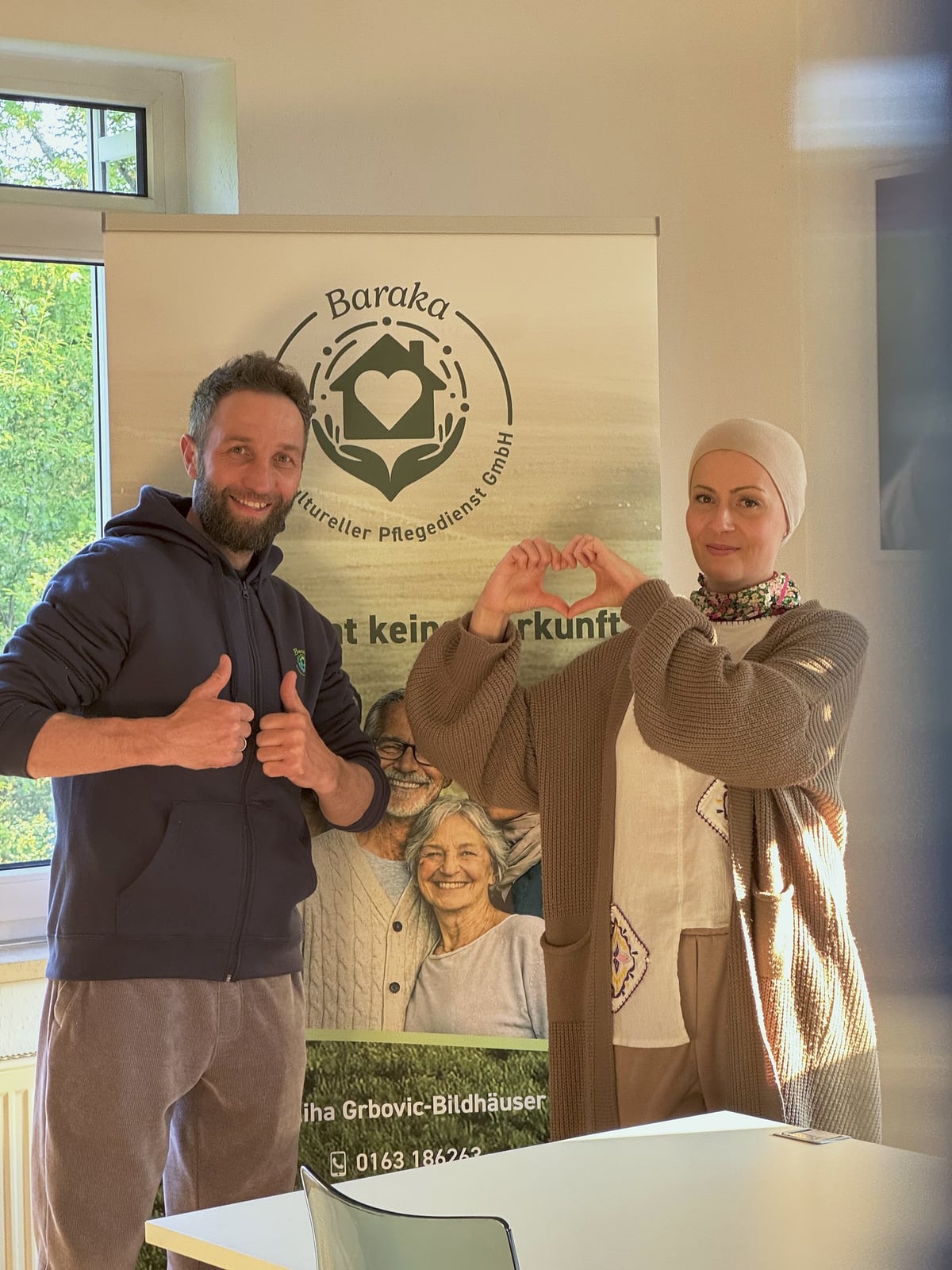 Patrick mit Daumen hoch und Meliha mit Herz-Geste vor dem Baraka-Roll-up